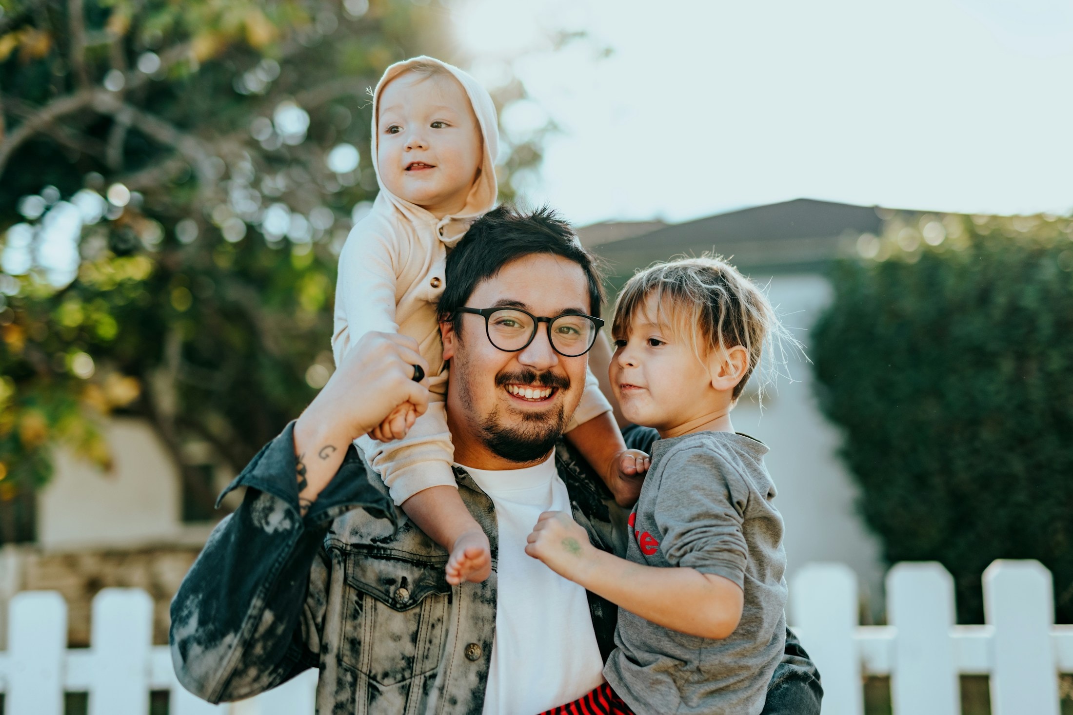Pai sorrindo com os dois filhos no colo
